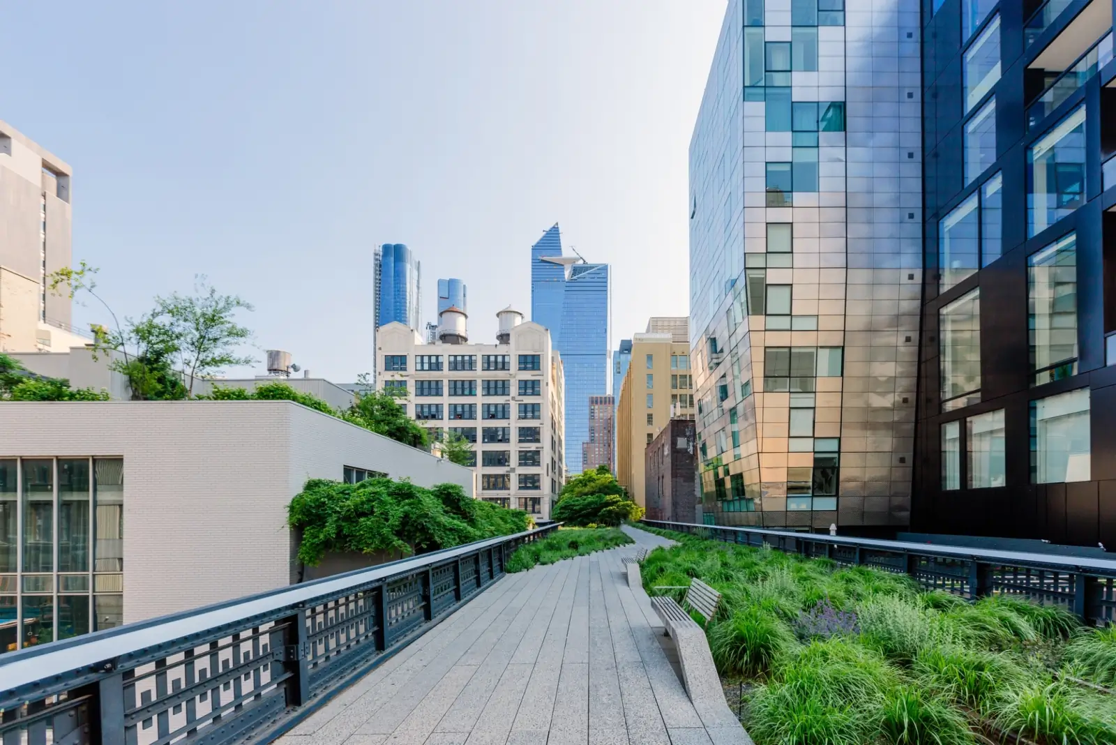 An elevated urban walkway lined with greenery and modern buildings on either side showcases the skyline, promoting energy efficiency. Adhering to The Passive House Energy Standard offers an elevated building quality on clear days in Canada.