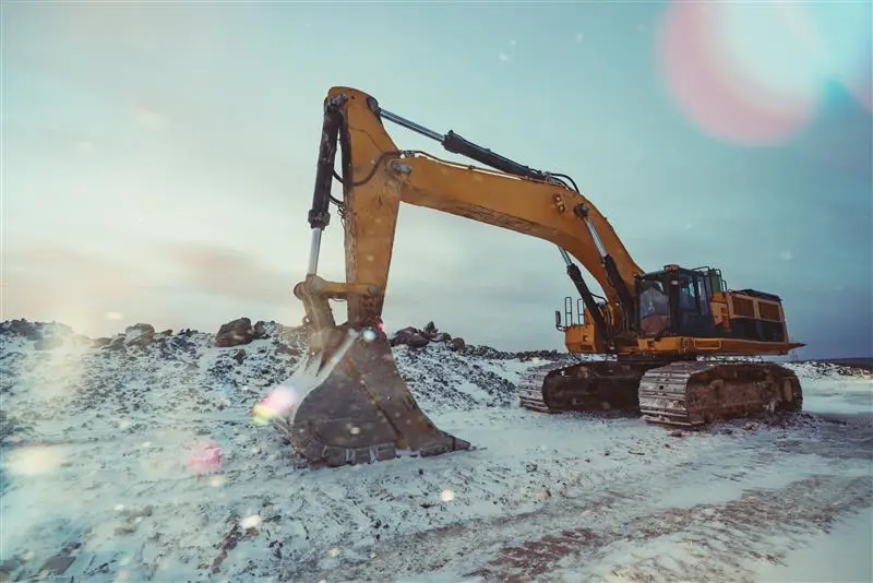 A yellow excavator in a northern community surrounded by snow breaking ground for a capital project